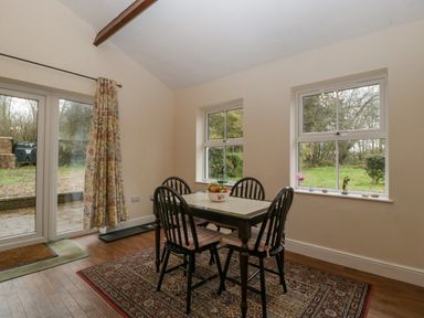 A dining area with a table and four chairs on a patterned rug next to two windows and glass doors in Heathfield Milverton