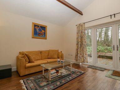 A living room with a tan sofa a glass coffee table with books on a rug and glass doors with floral curtains at Heathfield in Milverton