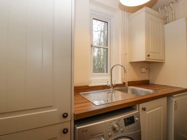 A kitchen area with a stainless steel sink and washing machine under a wooden countertop at Heathfield in Milverton
