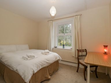 A bedroom with a bed a window with curtains a wooden desk and chair and a lamp on the desk at Heathfield in Milverton