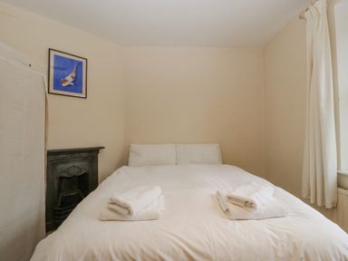 A bedroom with a bed with white linens and towels folded on it a black fireplace a framed picture on the wall and white curtains at Heathfield in Milverton