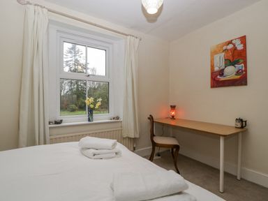 A bedroom with a bed, folded towels, a window with curtains, a wooden desk, a chair, a lamp, and a painting on the wall at Heathfield in Milverton