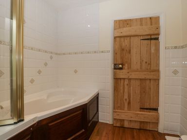 A bathroom with a corner bathtub wooden panel door and tiled walls at Heathfield in Milverton