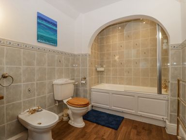 A bathroom with a bidet toilet with wooden seat bathtub with shower and blue rug at Heathfield in Milverton