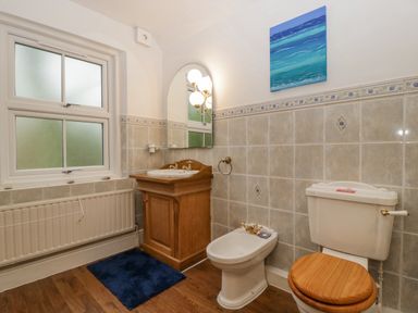 A bathroom with a toilet, bidet, wooden sink cabinet, mirror, and window at Heathfield in Milverton
