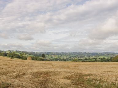 A harvested field with a stack of hay bales and distant hills under a cloudy sky at Heathfield in Milverton
