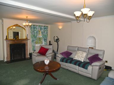 A living room with a fireplace armchair sofa round wooden table and exercise bike at Heathfield in Milverton