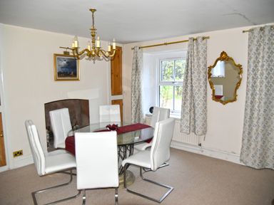 A dining room with a glass table and white chairs a gold chandelier a window with patterned curtains and a gold-framed mirror at Heathfield in Milverton
