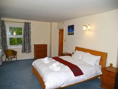 A bedroom with a double bed with white linens and folded towels near a window with curtains at Heathfield in Milverton