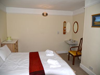 A bedroom with a bed with white linens and red runner a wooden chair a small dresser a sink and two mirrors at Heathfield in Milverton