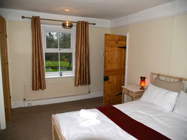 A bedroom with a double bed bedside table window with brown curtains and a wooden door at Heathfield in Milverton
