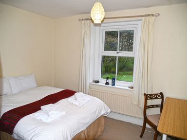 A bedroom with a bed with white linens and towels by a window with cream curtains and a wooden desk and chair at Heathfield in Milverton