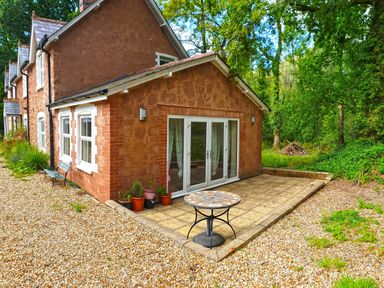 An outside view of a brick house with a patio and potted plants near a wooded area at Heathfield in Milverton