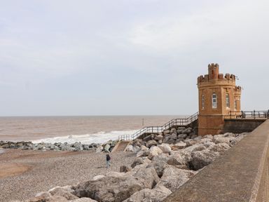 A pebble beach with large rocks and a small castle-like brick building by the sea at The Old Police House in Withernsea