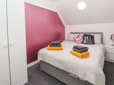 A bedroom with a double bed with folded towels pillows and a pink wall at The Old Police House in Withernsea