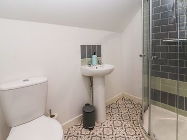 A bathroom with a toilet pedestal sink a small trash bin and a corner shower at The Old Police House in Withernsea