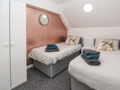 A bedroom with two single beds with folded towels and floral cushions a wardrobe and a round mirror on a pink wall at The Old Police House in Withernsea
