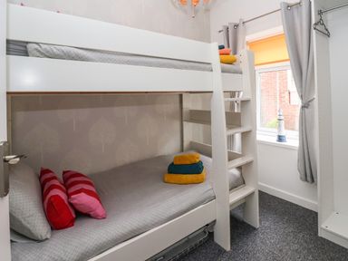 A small bedroom with white bunk beds, folded towels on the beds, a window with gray curtains, and an open wardrobe at The Old Police House in Withernsea
