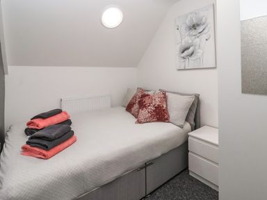 A small bedroom with a bed topped with folded towels and cushions a bedside table a wall painting and a round window at The Old Police House in Withernsea