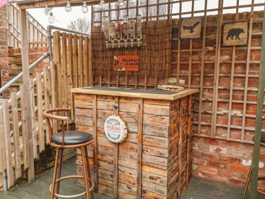 An outdoor wooden bar with liquor bottles mounted above and a bar stool in front at The Old Police House in Withernsea