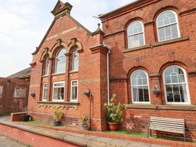 An exterior view of a red brick building with arched windows potted plants and a bench at The Old Police House in Withernsea