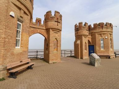 Two brick castle-like towers with battlements and archways by the sea with benches and a stone plaque at The Old Police House in Withernsea
