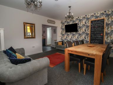 A living room with sofas a wooden dining table with chairs a wall-mounted television and a chalkboard at The Old Police House in Withernsea