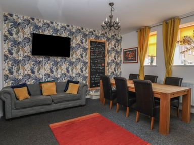 A living room with a grey sofa and cushions a wooden dining table with black chairs and yellow curtains at The Old Police House in Withernsea