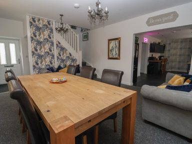 A dining area with a wooden table and leather chairs next to a sitting area with a sofa and cushions at The Old Police House in Withernsea