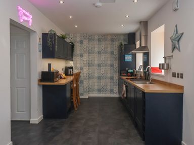 A kitchen with dark cabinets wooden countertops patterned tile backsplash and bar stools at The Old Police House in Withernsea