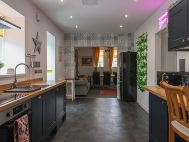 A kitchen with black cabinets wooden countertops a stainless steel sink and oven a black refrigerator and a dining area visible through a tiled doorway at The Old Police House in Withernsea