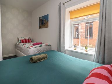 A bedroom with two beds a window with curtains and small decorative figurines on the sill at The Old Police House in Withernsea
