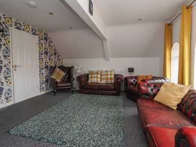 A living room with red leather sofas a chair yellow curtains and a floral wallpaper at The Old Police House in Withernsea