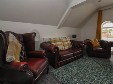 A sitting room with leather armchairs and a sofa with cushions and a window with curtains at The Old Police House in Withernsea