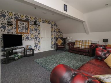 A living room with leather sofas a TV stand with books and a floral wallpapered wall at The Old Police House in Withernsea