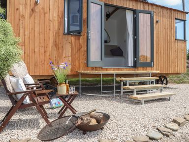 An outdoor seating area with two wooden chairs a small table with a vase of flowers near a wooden building with open double doors at Little Pip in Gulval