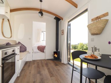 A small kitchen and dining area with a wood stove and an open door showing a garden at Little Pip in Gulval