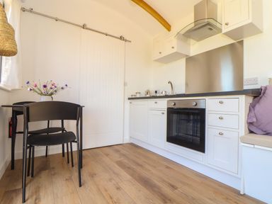A kitchen with white cabinets black countertop black dining table and chairs wooden floor at Little Pip in Gulval