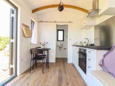 A small kitchen with white cabinets a black countertop a round table with two chairs and a sliding door at Little Pip in Gulval