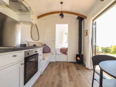 A small kitchen and dining area with a black wood stove and doorway to a bedroom at Little Pip in Gulval