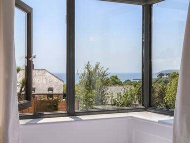 A window with one open pane showing a view of rooftops trees and the sea at Little Pip in Gulval