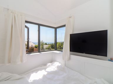 A bedroom with a bed a wall-mounted TV and corner windows with curtains at Little Pip in Gulval