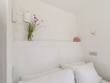 A bed with white pillows a vase with flowers and a pink clock on the headboard at Little Pip in Gulval