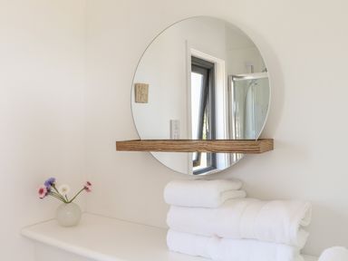 A bathroom counter with folded white towels a small vase with flowers and a round mirror at Little Pip in Gulval