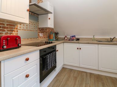 A kitchen with white cabinets a black oven a red toaster a sink and items on the counter at Valley Lodge 55 in Callington near Gunnislake
