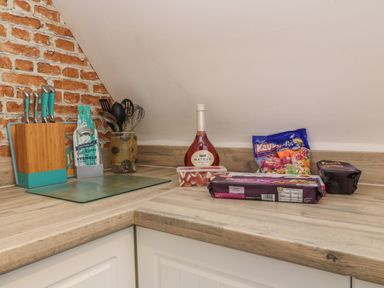 A kitchen countertop with a knife block utensils in a jar a bottle of Mateus wine and snacks at Valley Lodge 55 Callington near Gunnislake