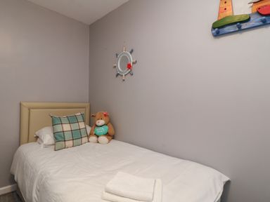 A single bed with a headboard and a plaid pillow a teddy bear and folded towels on the bed in a small room at Valley Lodge 55 in Callington near Gunnislake