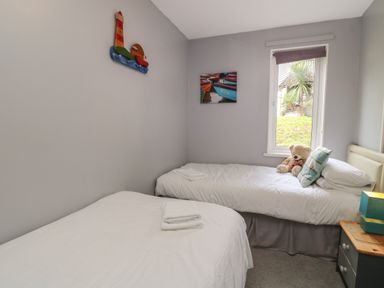 A bedroom with two single beds a teddy bear on one bed and a window showing greenery at Valley Lodge 55 Callington near Gunnislake