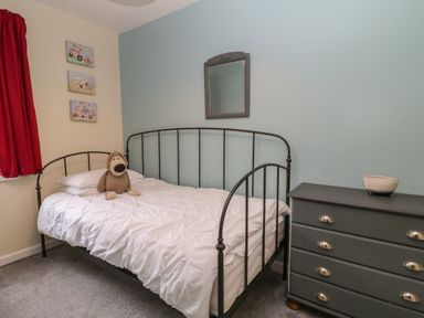 A bedroom with a metal framed bed and a stuffed toy on the bed a gray chest of drawers with a bowl on top and three small pictures on the wall at Valley Lodge 55 Callington near Gunnislake
