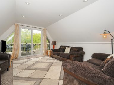A living room with two brown sofas a patterned rug a floor lamp and sliding glass doors leading to a balcony at Valley Lodge 55 Callington near Gunnislake